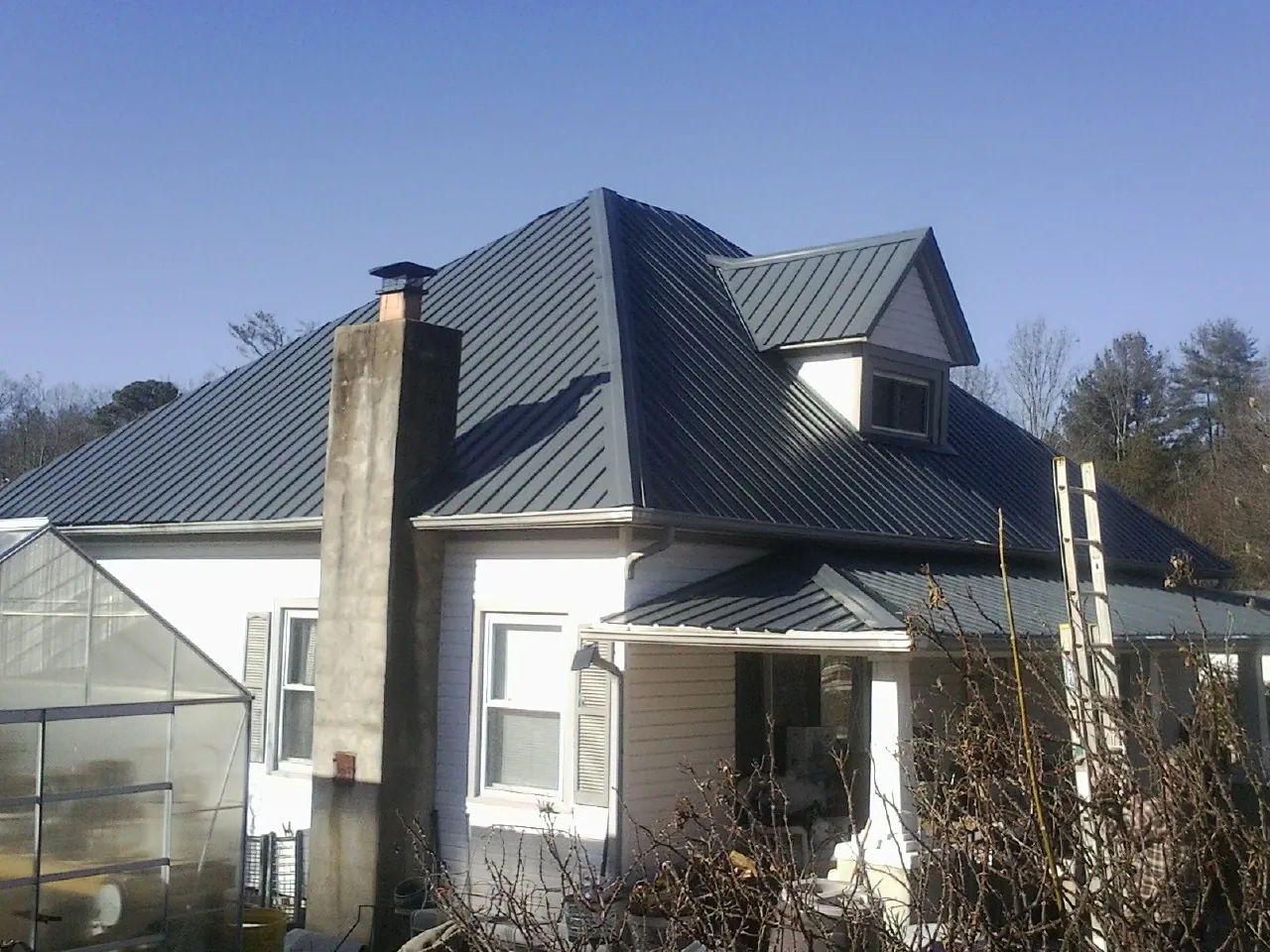 Dark blue standing seam metal roof on a white farmhouse with dormer — Slate & Tile Roof Repair by Roofing Brothers in Roslyn Heights