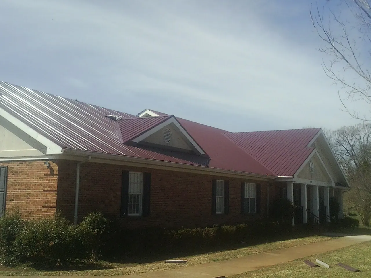 Red metal roof with gabled entries on a long brick building, from a Hail Damage Roof Repair job in Roslyn Heights