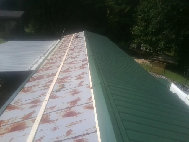 Old rusted panels beside newly installed green metal roofing — Wind Damage Roof Repair by Roofing Brothers in Roslyn Heights