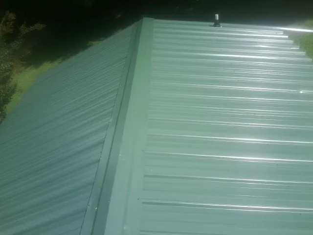 New green metal panels meeting at the ridge of a roof — Flat Roof Repair work by our crew in Roslyn Heights