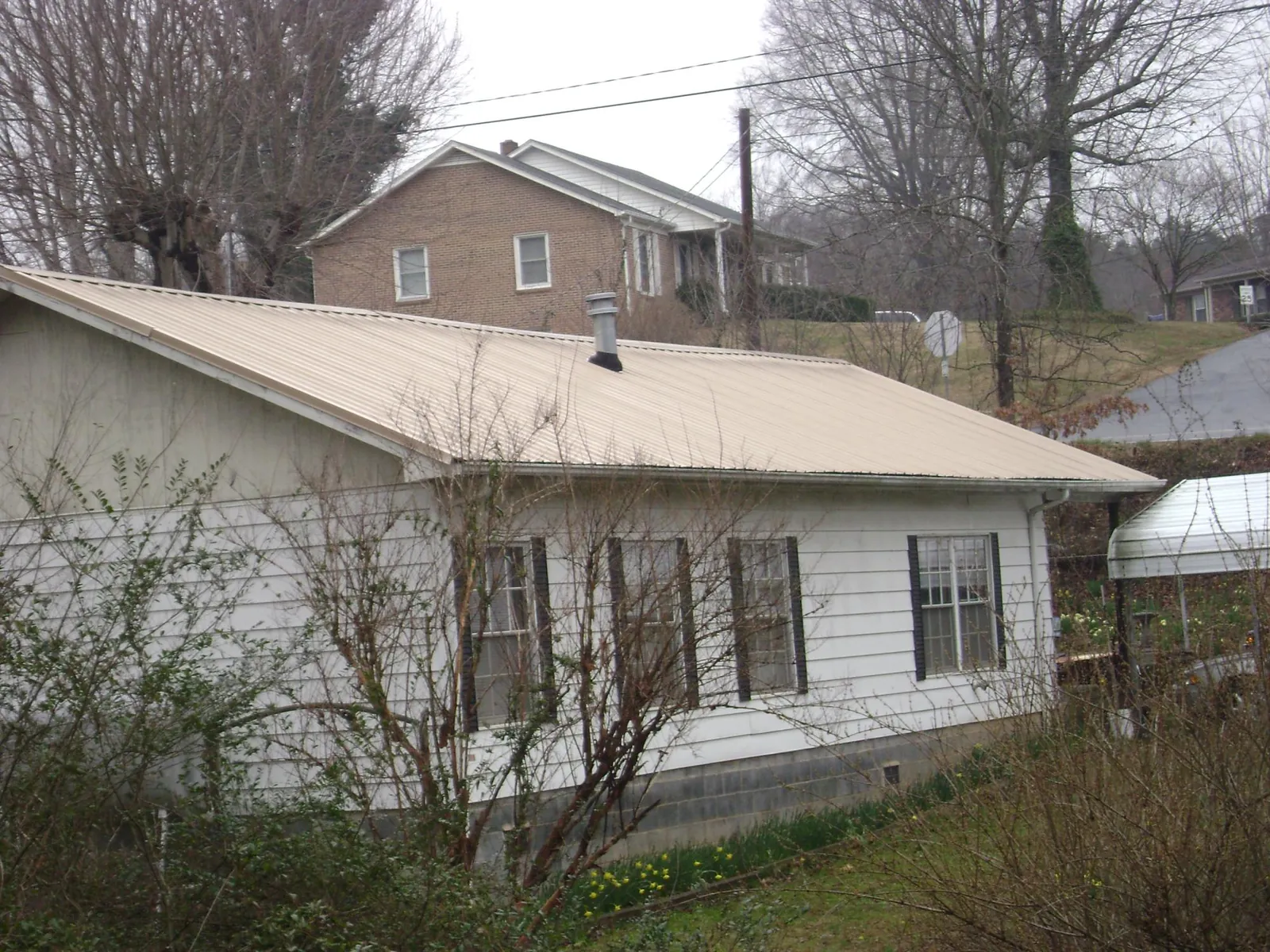 Tan metal roof on a white sided house set into a hillside — Commercial Roofing by Roofing Brothers in Roslyn Heights