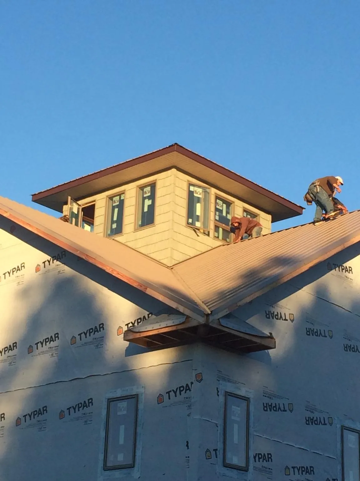 Roofers working around a rooftop cupola on a new metal roof at sunset — Roof Waterproofing in Roslyn Heights by Roofing Brothers